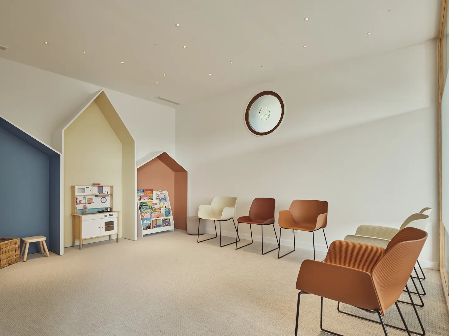 Sala de espera infantil con casitas de colores, cocinita de juguete y estantería de cuentos